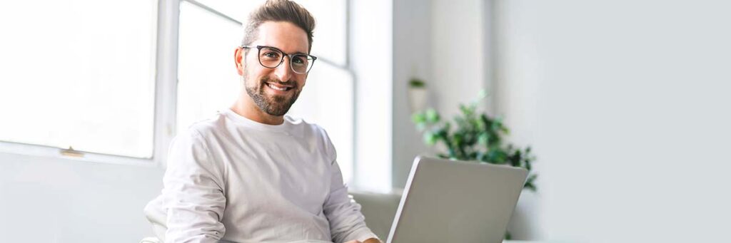 Mann sitzt am Laptop und lächelt in die Kamera