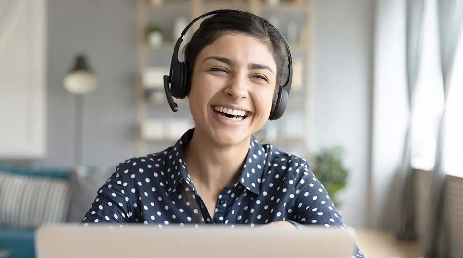 Eine Frau mit Headset sitzt hinter ihrem Laptop und lächelt zufrieden.