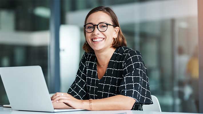 Das Titelbild zeigt eine lächelnde Frau am Computer und steht sinnbildlich für einen positiven beruflichen Neustart nach Krankheit oder Reha durch Neuorientierung und Qualifizierung.