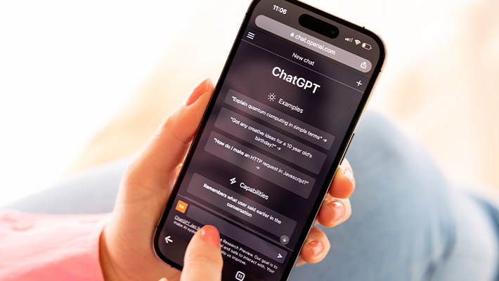 Zu sehen ist eine weibliche Person, die auf ihr Handy tippt, auf dem Smartphone-Bildschirm sieht man einen Chat von ChatGPT.