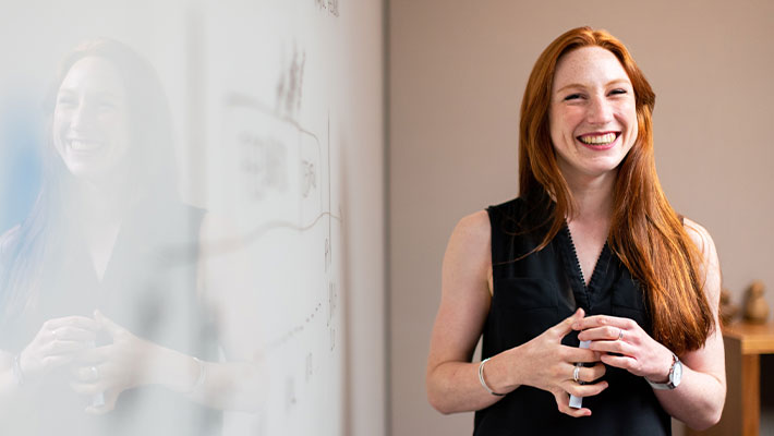 Eine Frau steht vor einem Whitebord und lächelt, zu den Aufgaben einer/eines SAP-Berter:in gehört auch die Schulung von Menschen, die mit der Software arbeiten.