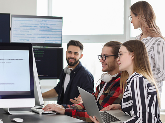 Eine Gruppe Teilnehmer sitzt in einer Umschulung vor dem Computer und erarbeiten eine Gruppenaufgabe.