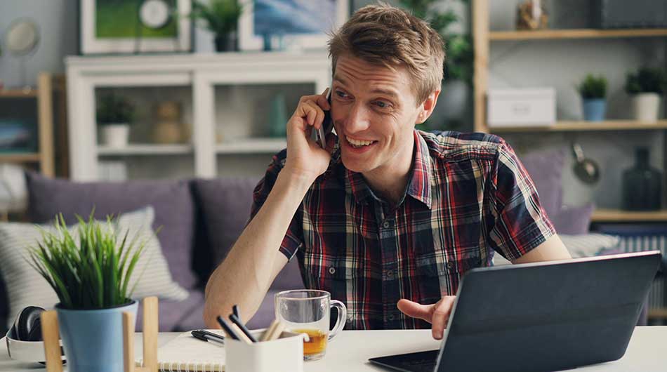 Ein Mann sitzt an seinem Laptop und telefoniert.